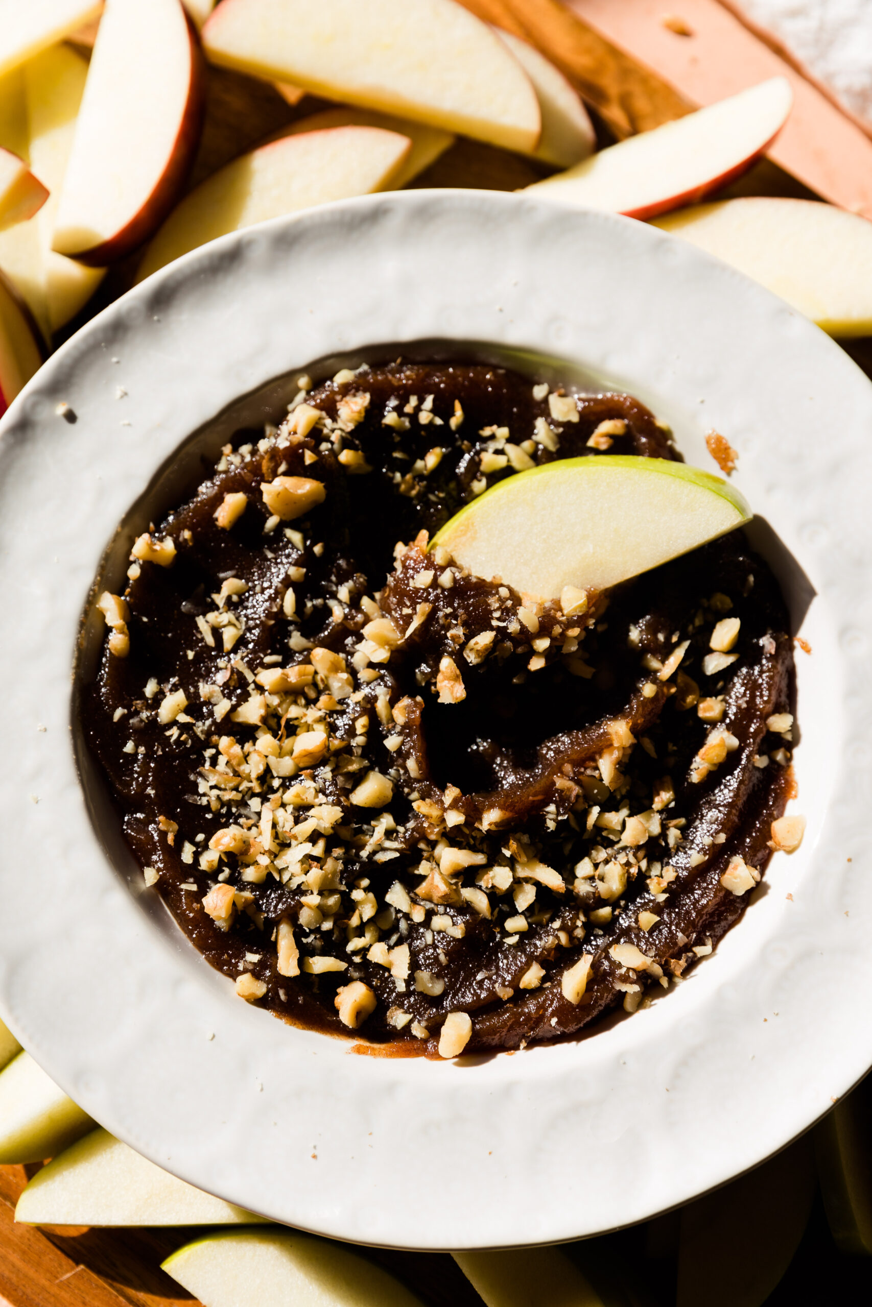 White bowl with date caramel and apple slices around the bowl.