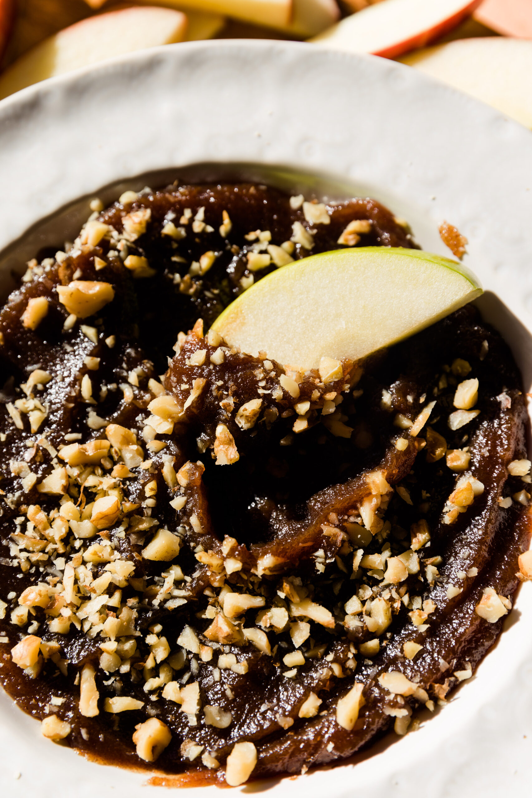 Apple slice dipped in homemade caramel apple dip with chopped walnuts on top.