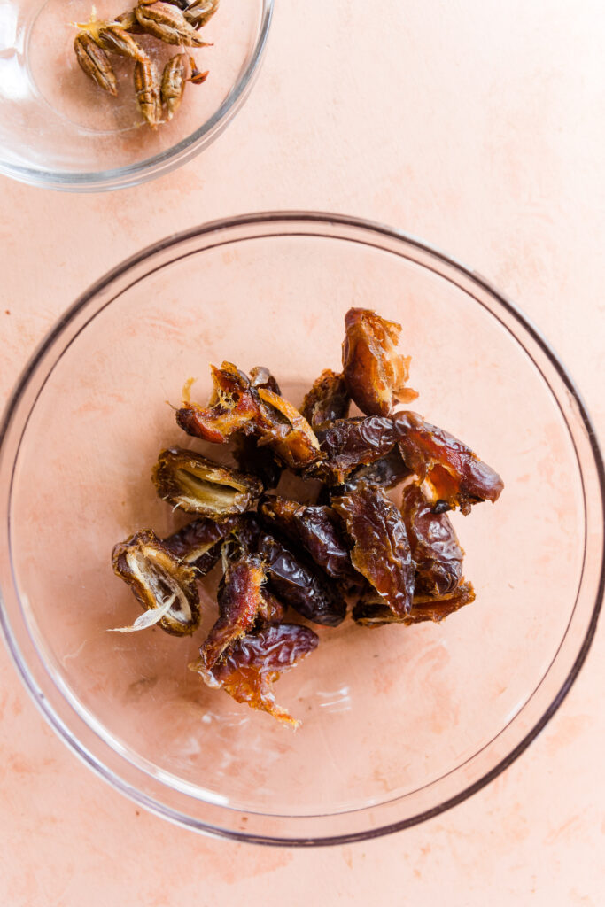 Pitted dates in a glass bowl with small bowl full of pits next to it.