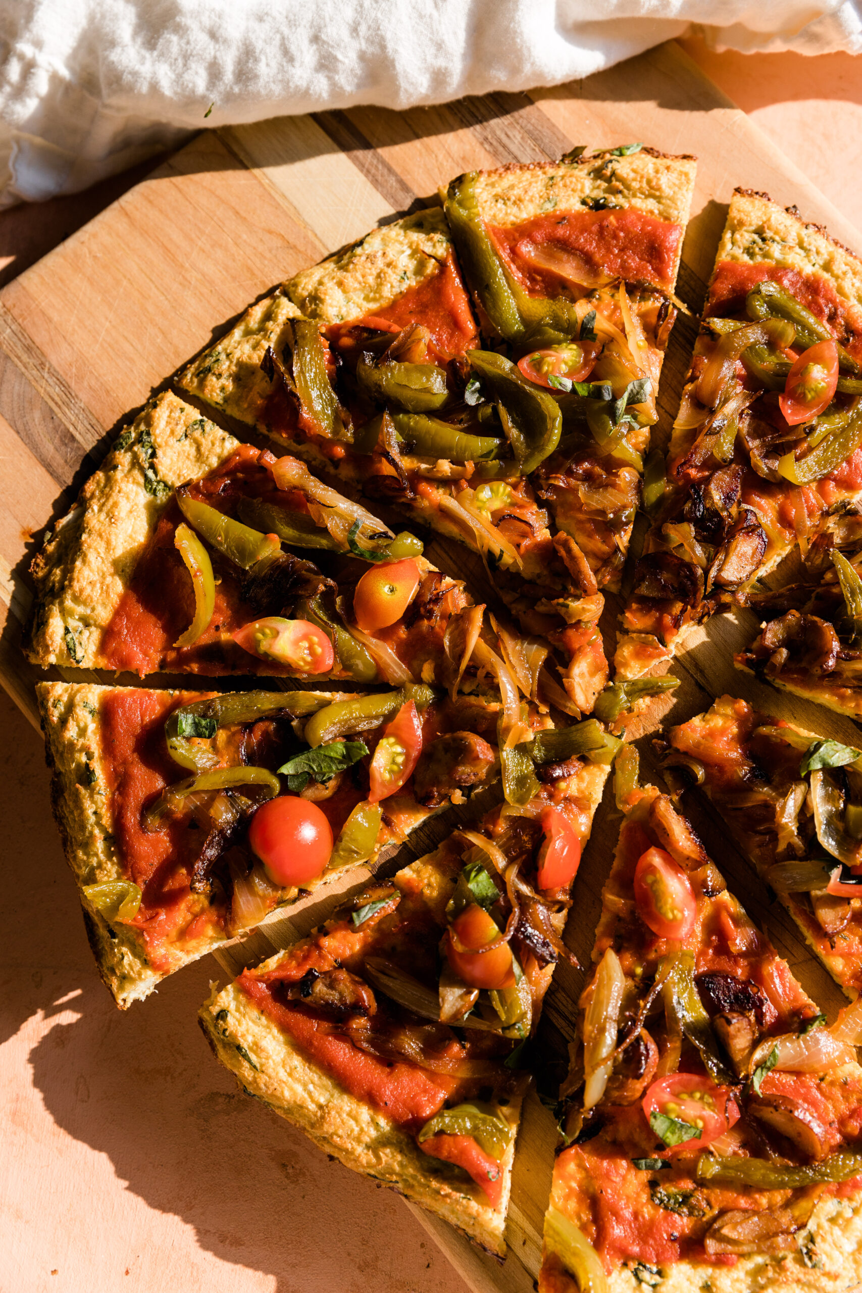 Cauliflower pizza cut into individual pieces on wooden cutting board.