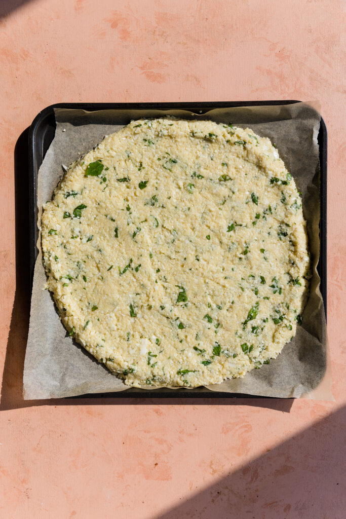 Cauliflower pizza crust dough spread into a circle on a parchment paper lined baking sheet.