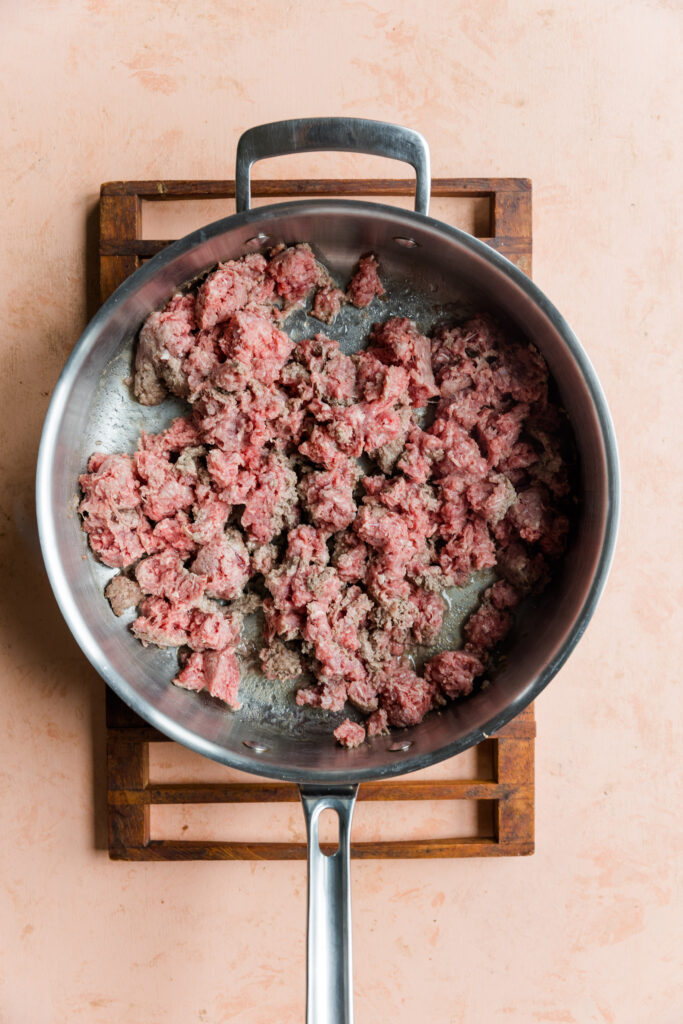 Ground beef cooking in a stainless steel pan.