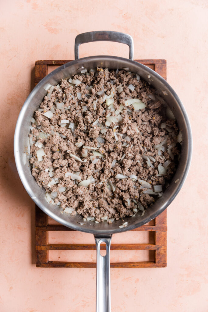 Ground beef with onions, garlic, salt, and pepper cooking in a pan.
