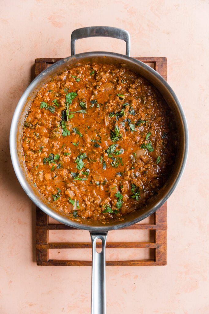 Cooked meat sauce in a large pan with fresh basil on top.