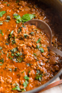 Ladle scooping out meat sauce from the pot.