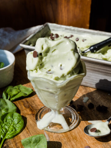 Mint chocolate chip ice cream in a glass cup with a spoonful taken out.