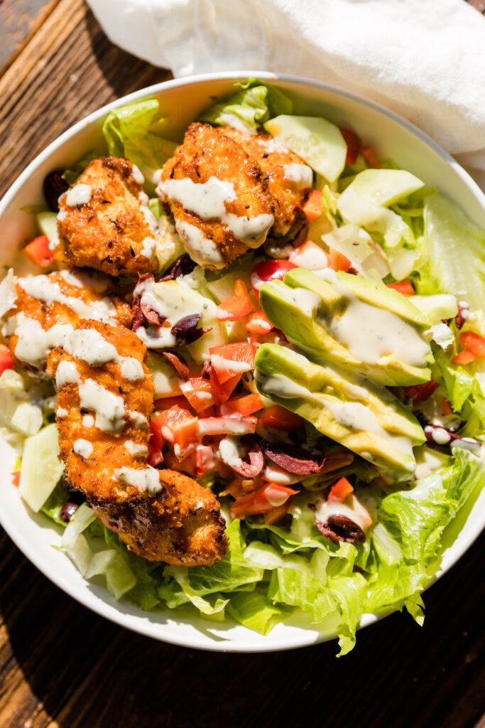Finished buffalo chicken salad in white bowl topped with ranch dressing.