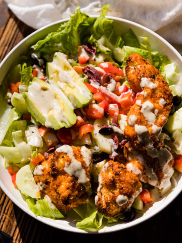 Close up picture of crispy buffalo chicken salad in white ceramic bowl on wood board.