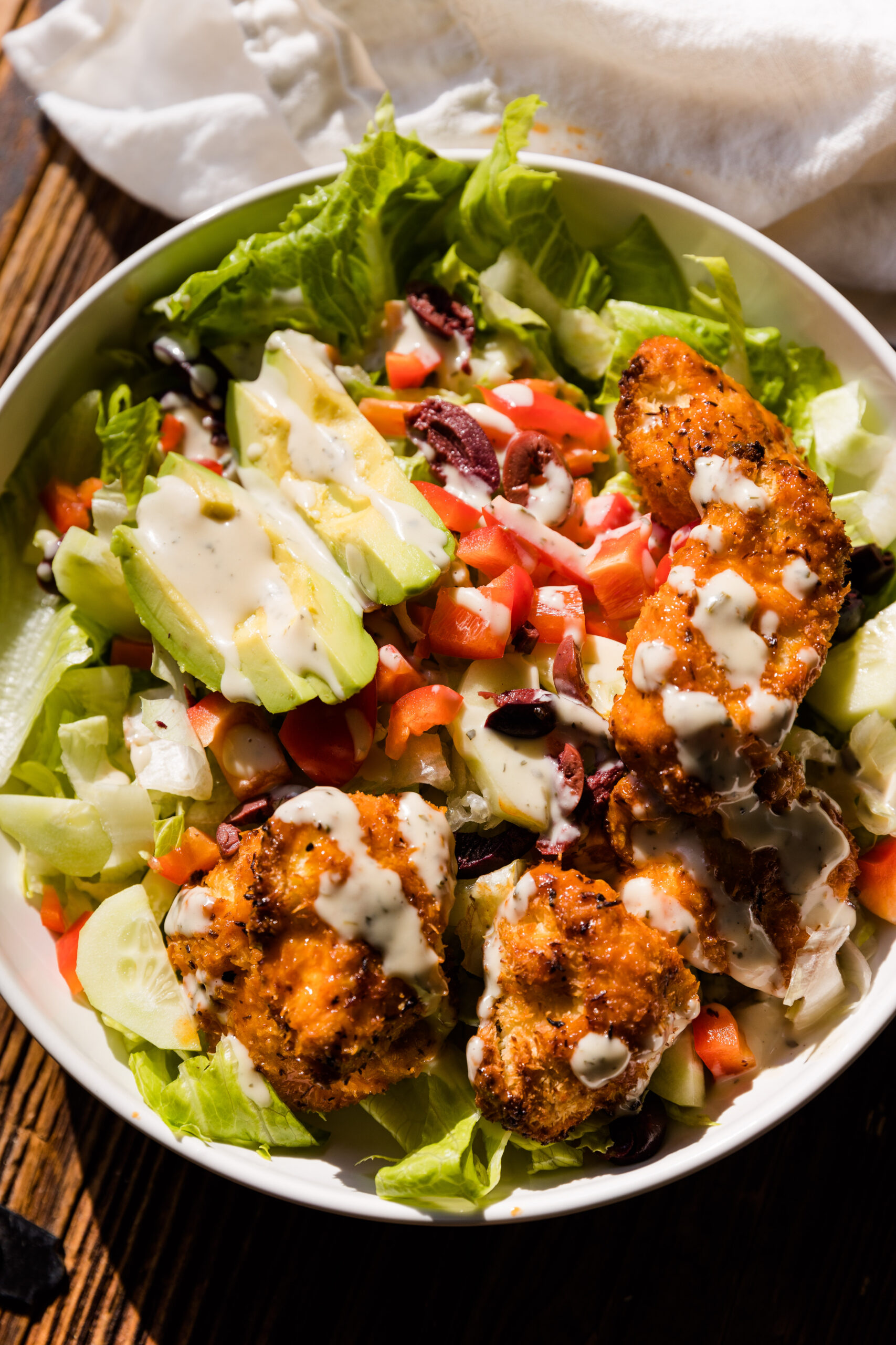 Close up picture of crispy buffalo chicken salad in white ceramic bowl on wood board.