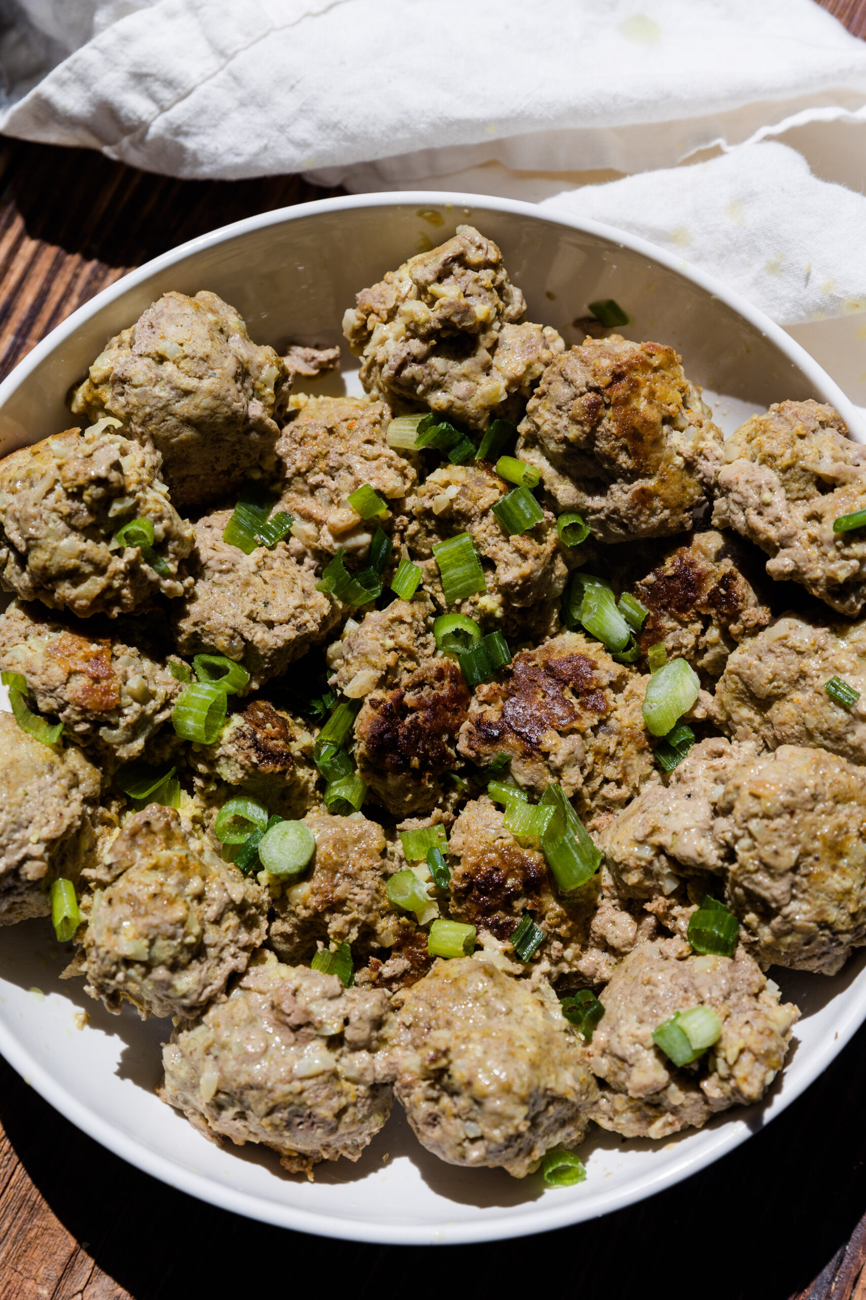 Ginger curry meatballs on a white plate with green onion garnish.