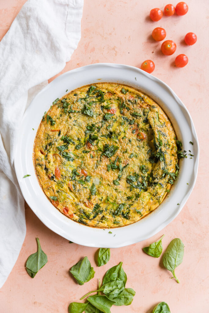 Cooked frittata in round baking dish with fresh vegetables on the side.