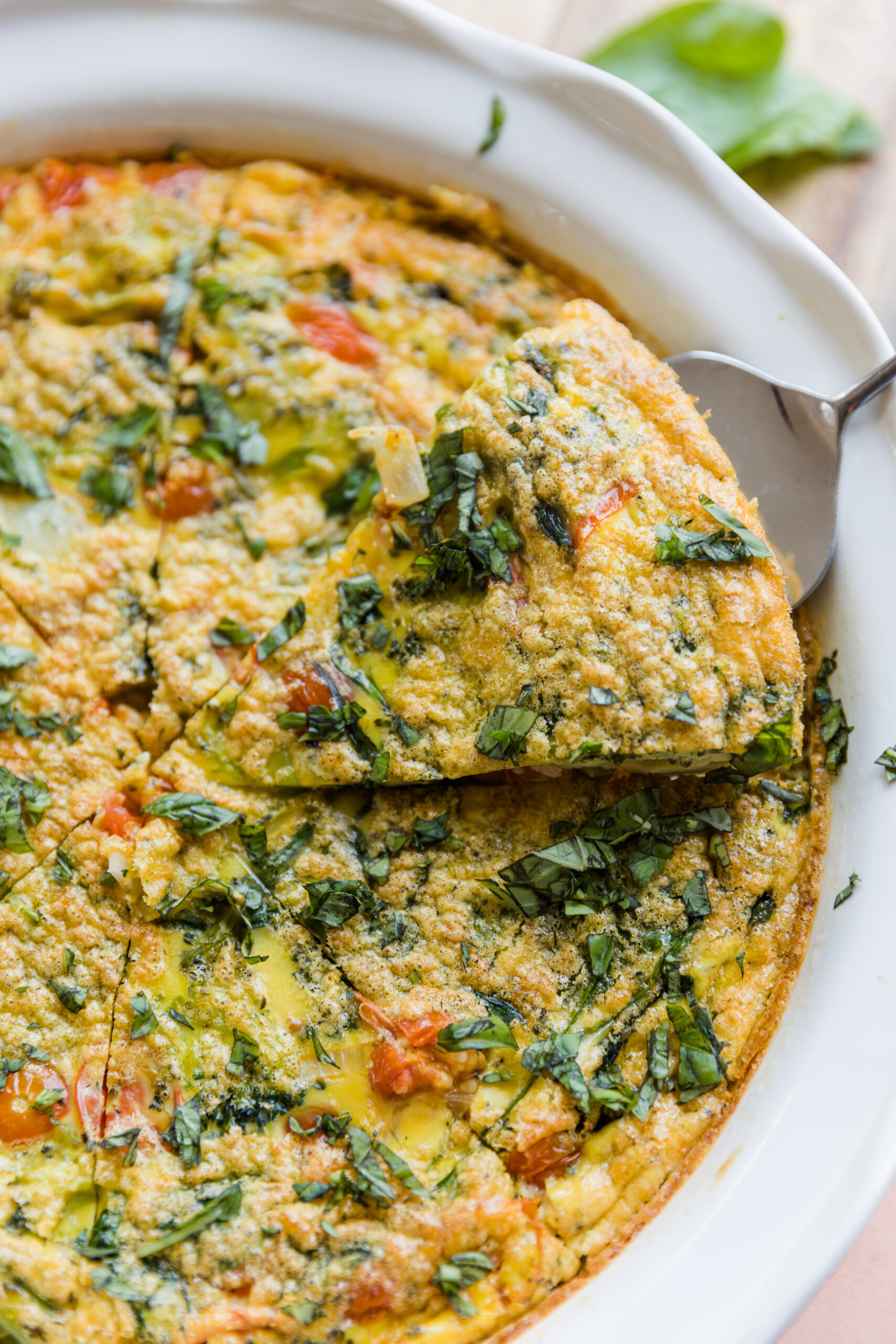 A large slice of the vegetable frittata held up by a serving tool.