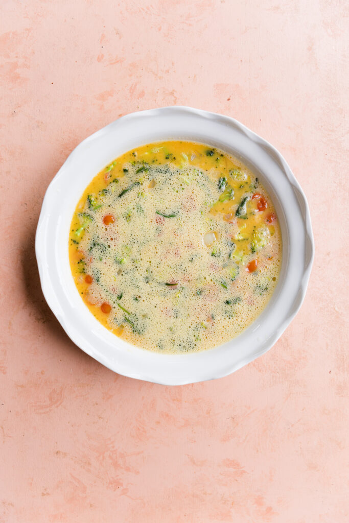 Cooked vegetables and egg mixture in round baking dish.