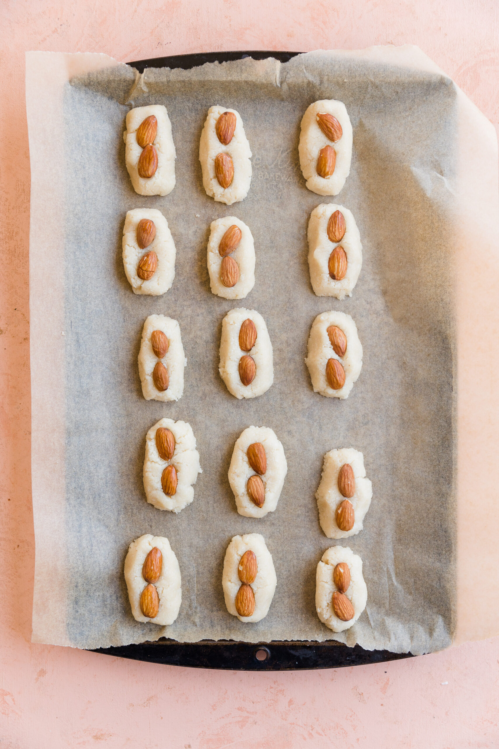 15 coconut candy bars on a parchment paper lined baking sheet with two almonds on each one.