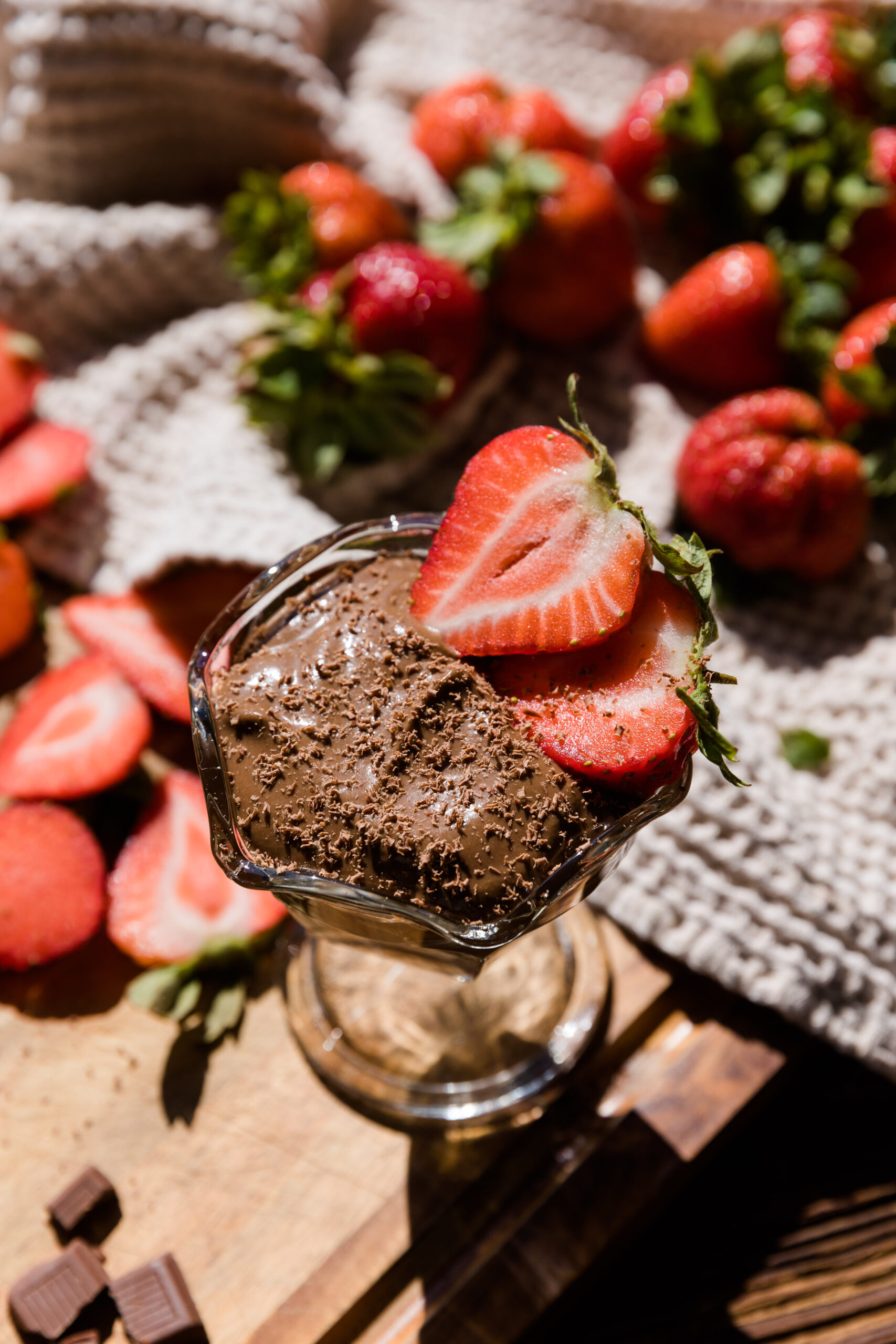 Fresh cut strawberries on a cutting board with a tall glass jar filled with chocolate avocado pudding with shaved chocolate on top.