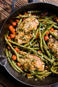 Chicken breast with green beans and tomatoes in a cast iron skillet.