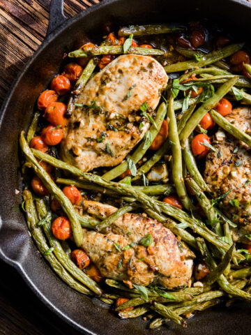Chicken breast with green beans and tomatoes in a cast iron skillet.