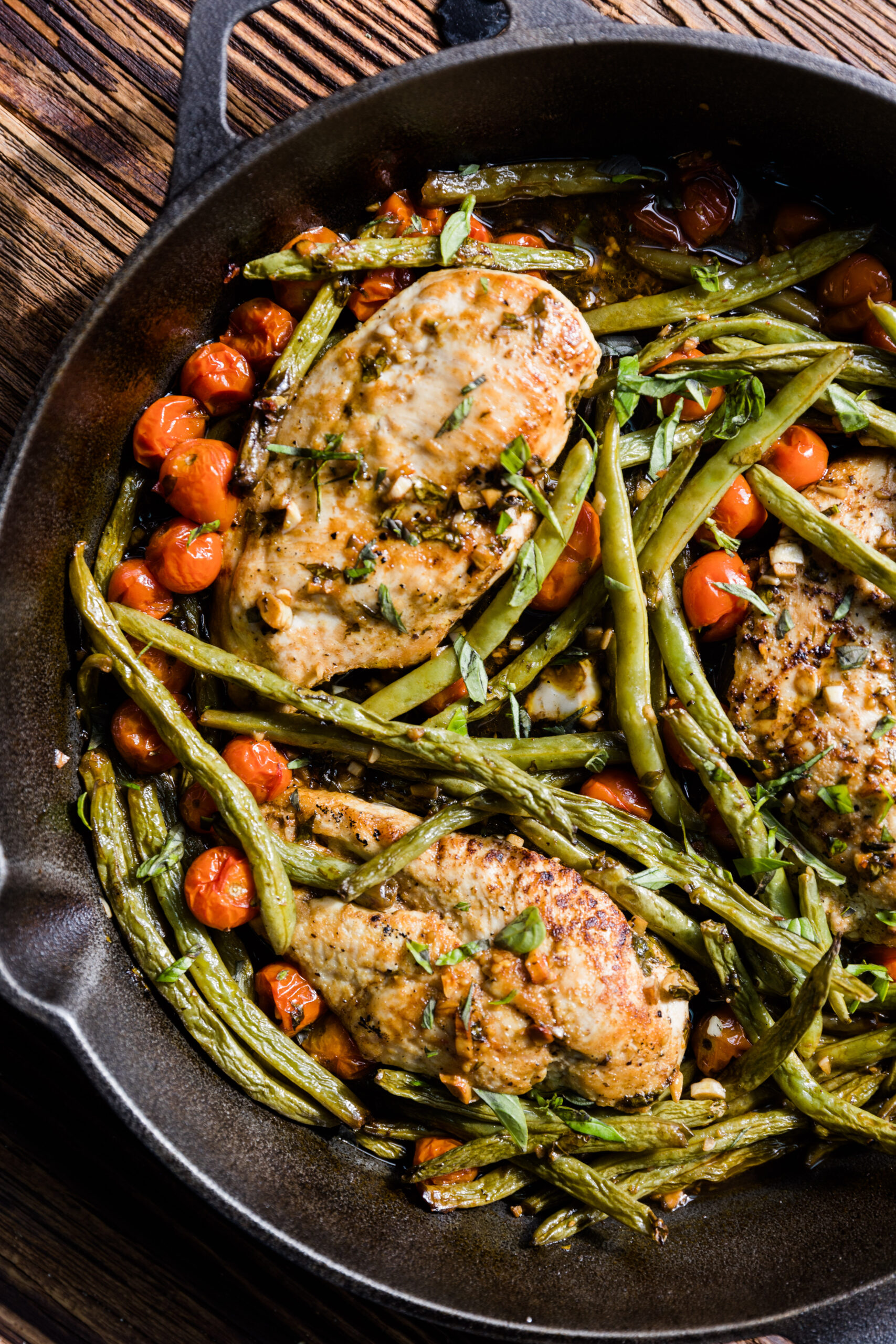 Chicken breast with green beans and tomatoes in a cast iron skillet.