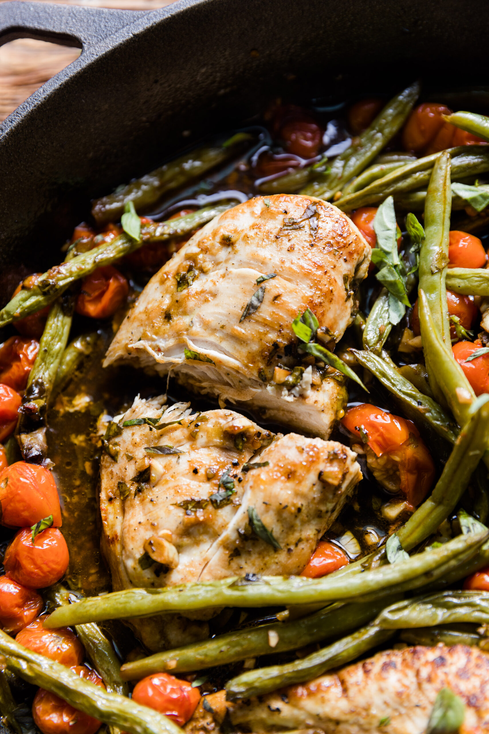 Cooked chicken breast cut in half with fresh basil on top.