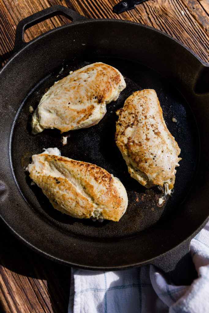 Chicken breast cooking in cast iron skillet.