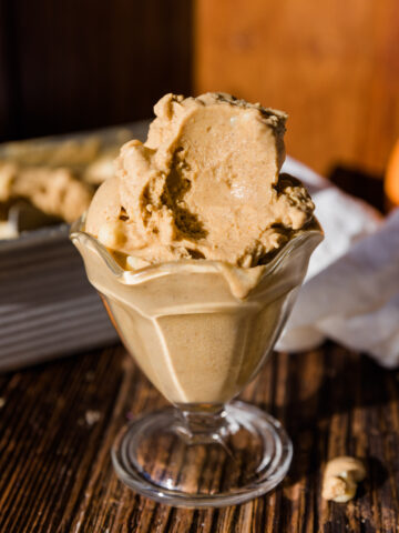 Glass ice cream cup with a large scoop of pumpkin ice cream that has a big spoonful taken out.