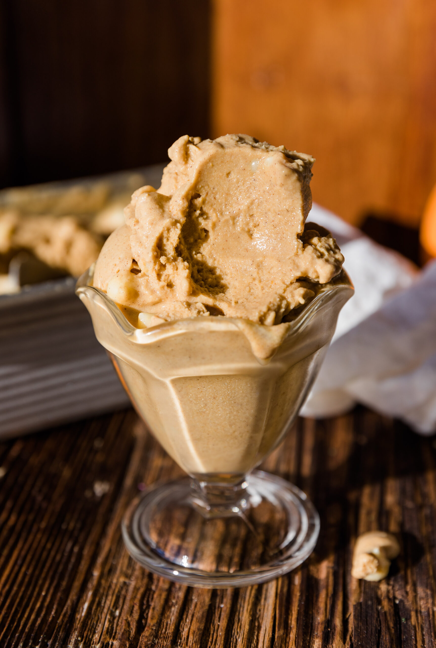 Glass ice cream cup with a large scoop of pumpkin ice cream that has a big spoonful taken out.