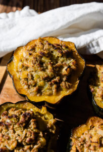 Stuffed Acorn squash on a wooden board with a white kitchen towel.