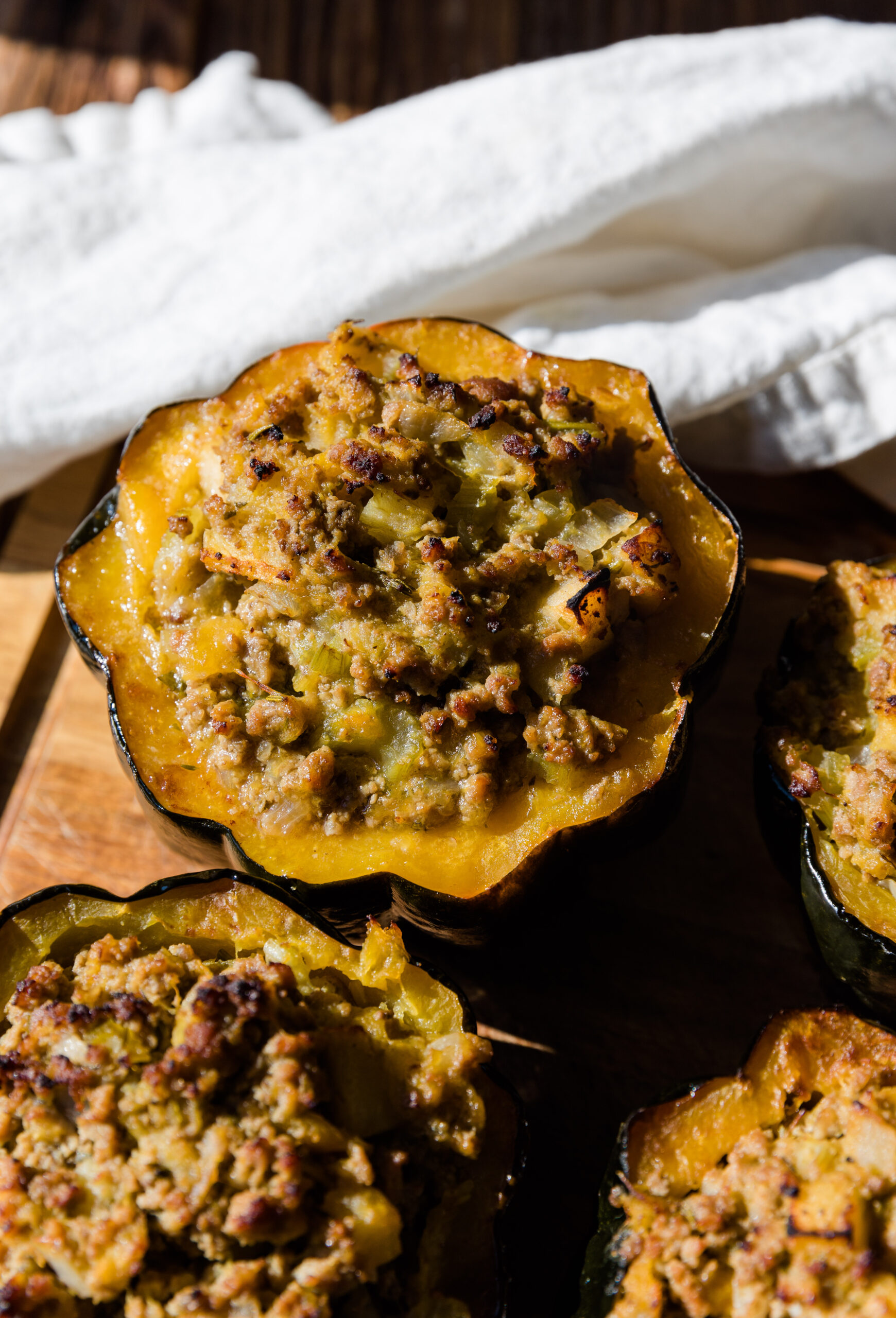 Stuffed Acorn squash on a wooden board with a white kitchen towel.