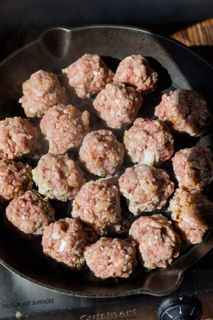 Apple herb meatballs cooking in cast iron skillet.