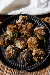 Apple and herb meatballs on a black plate with fresh thyme on top.