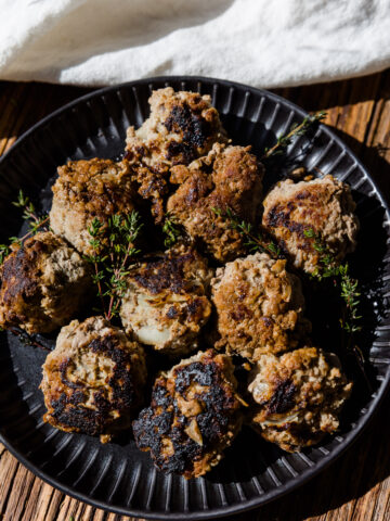 Apple and herb meatballs on a black plate with fresh thyme on top.
