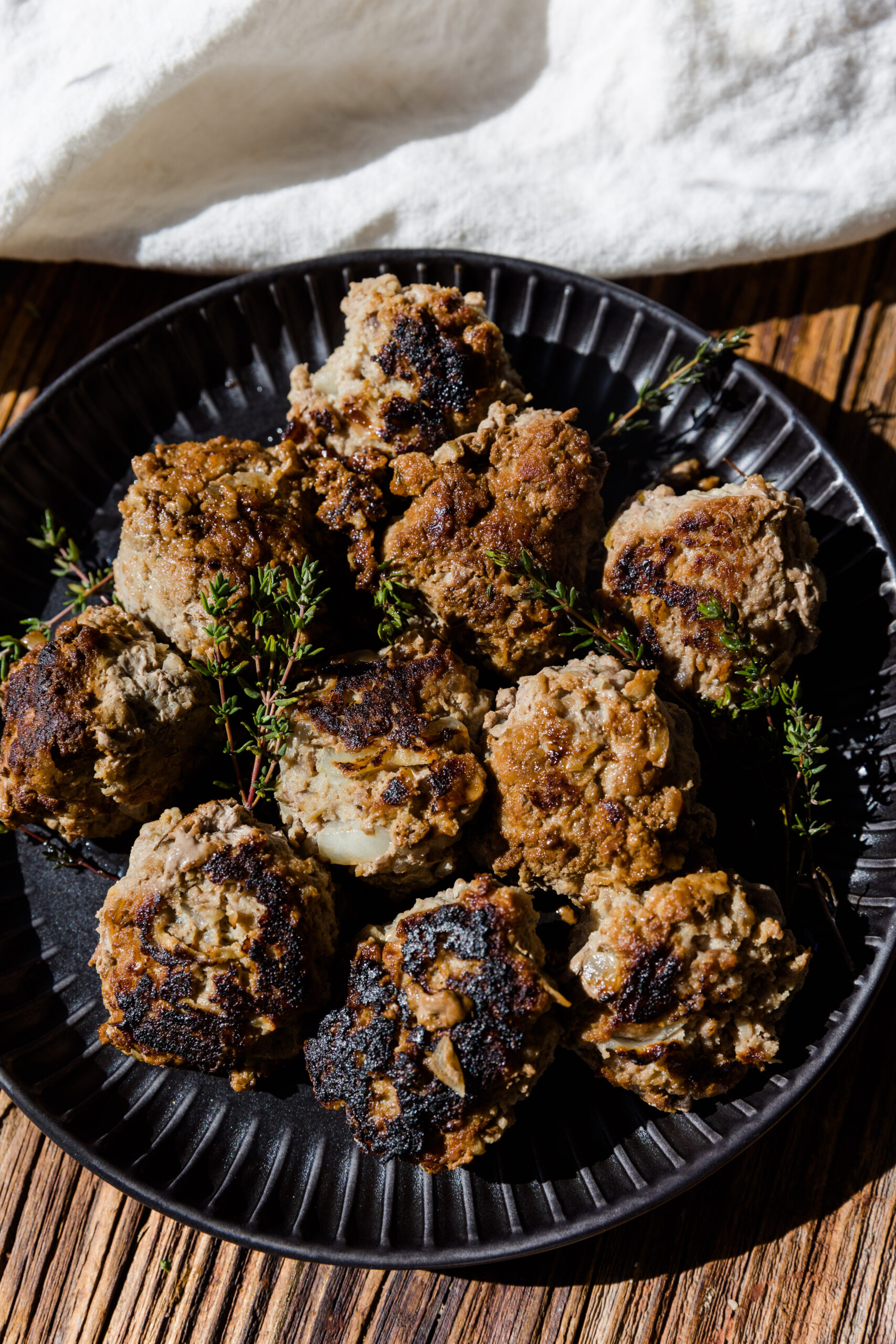 Apple and herb meatballs on a black plate with fresh thyme on top.
