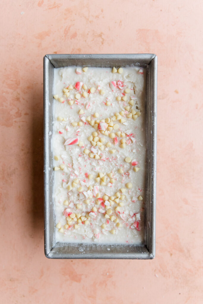 Peppermint ice cream in metal loaf pan with crushed candy canes and white chocolate chips.