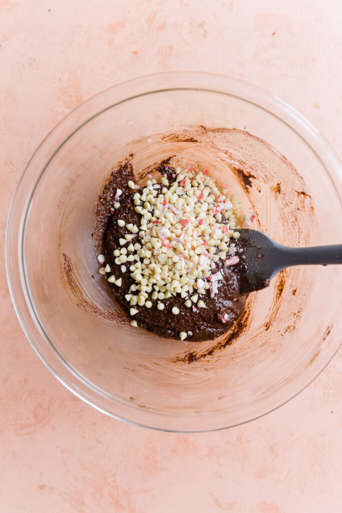 Chocolate peppermint cookie dough in a bowl topped with white chocolate chips and crushed candy canes.