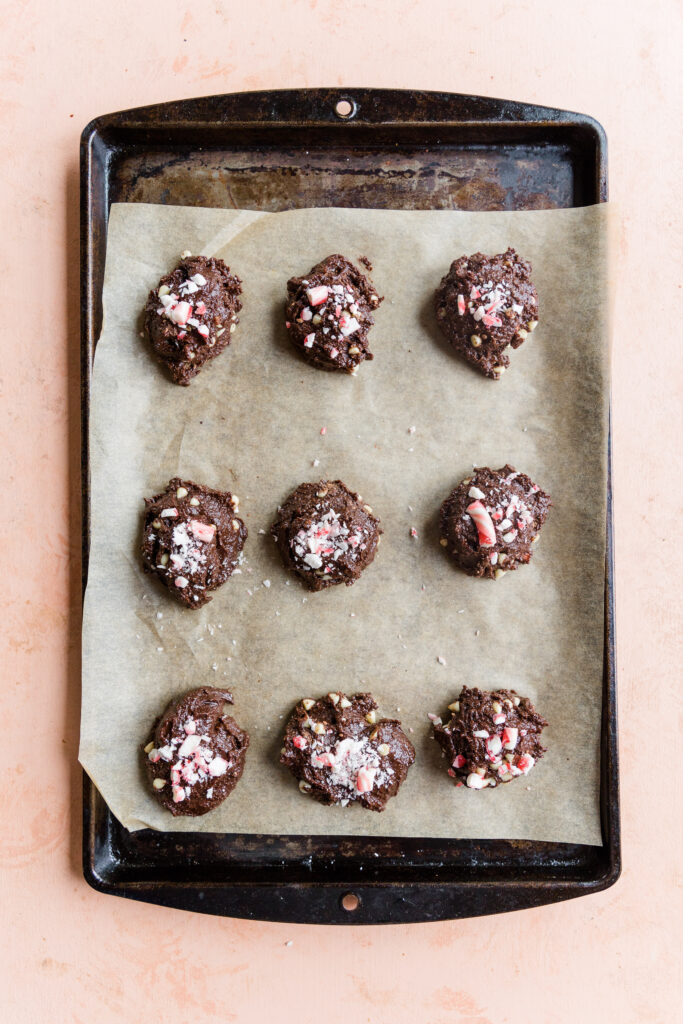 Nine chocolate peppermint cookie dough balls on a parchment paper lined baking sheet.