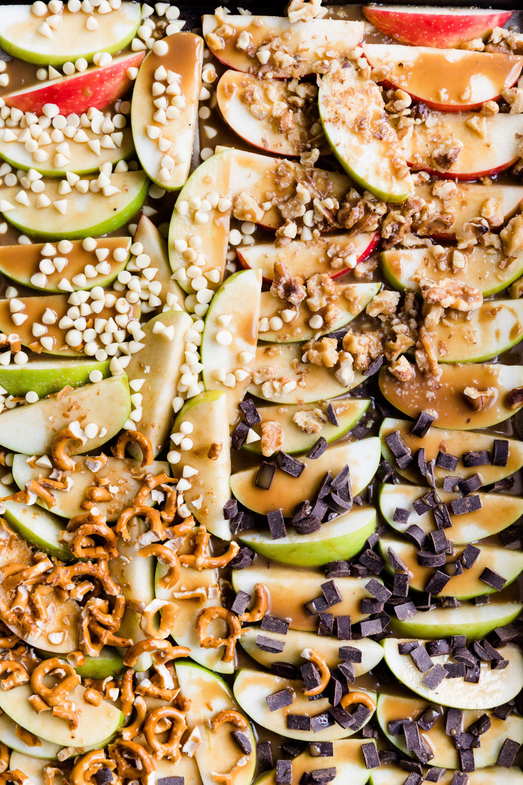 Close up picture of sheet pan caramel apple slices with chocolate, pretzels, and walnuts on top.