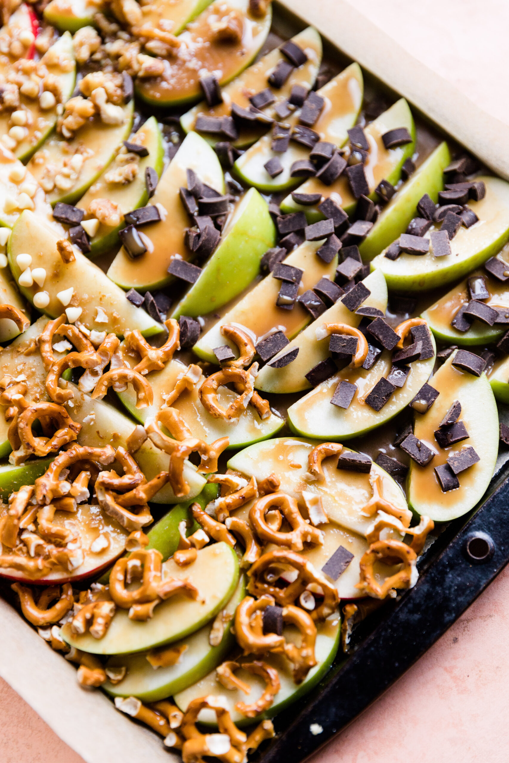 Close up picture of green apple slices with dairy free caramel drizzled on top with chocolate and pretzels.