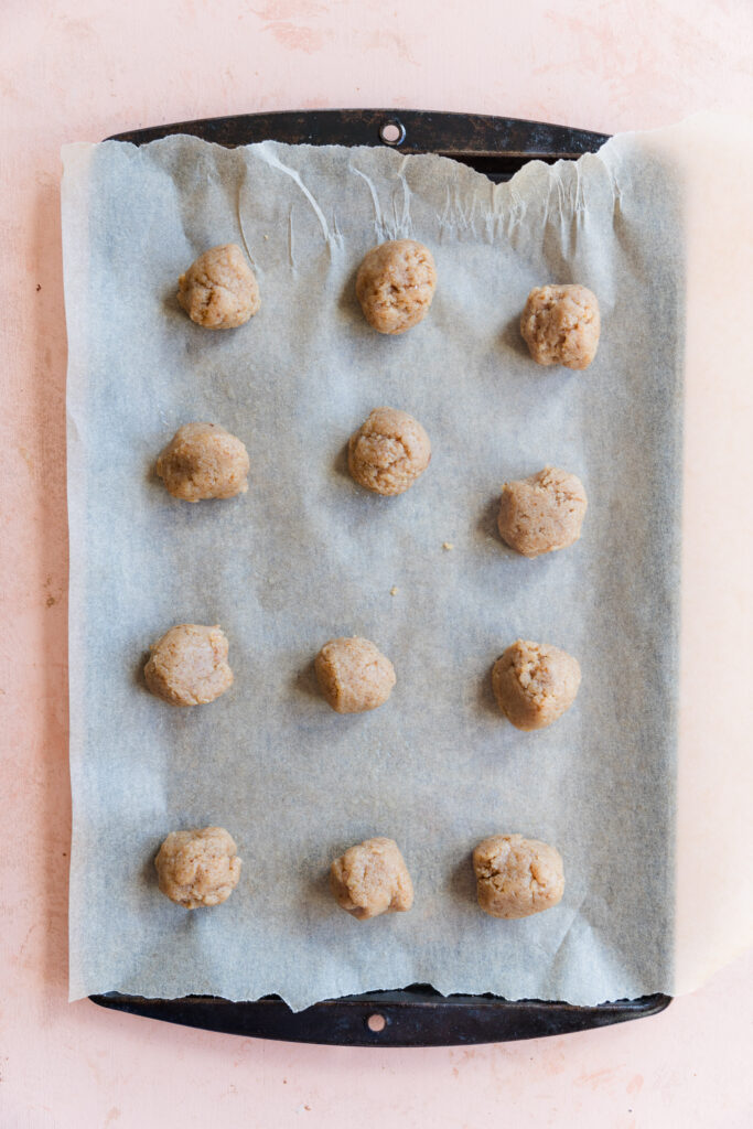Cookie dough balls on parchment paper lined baking sheet.