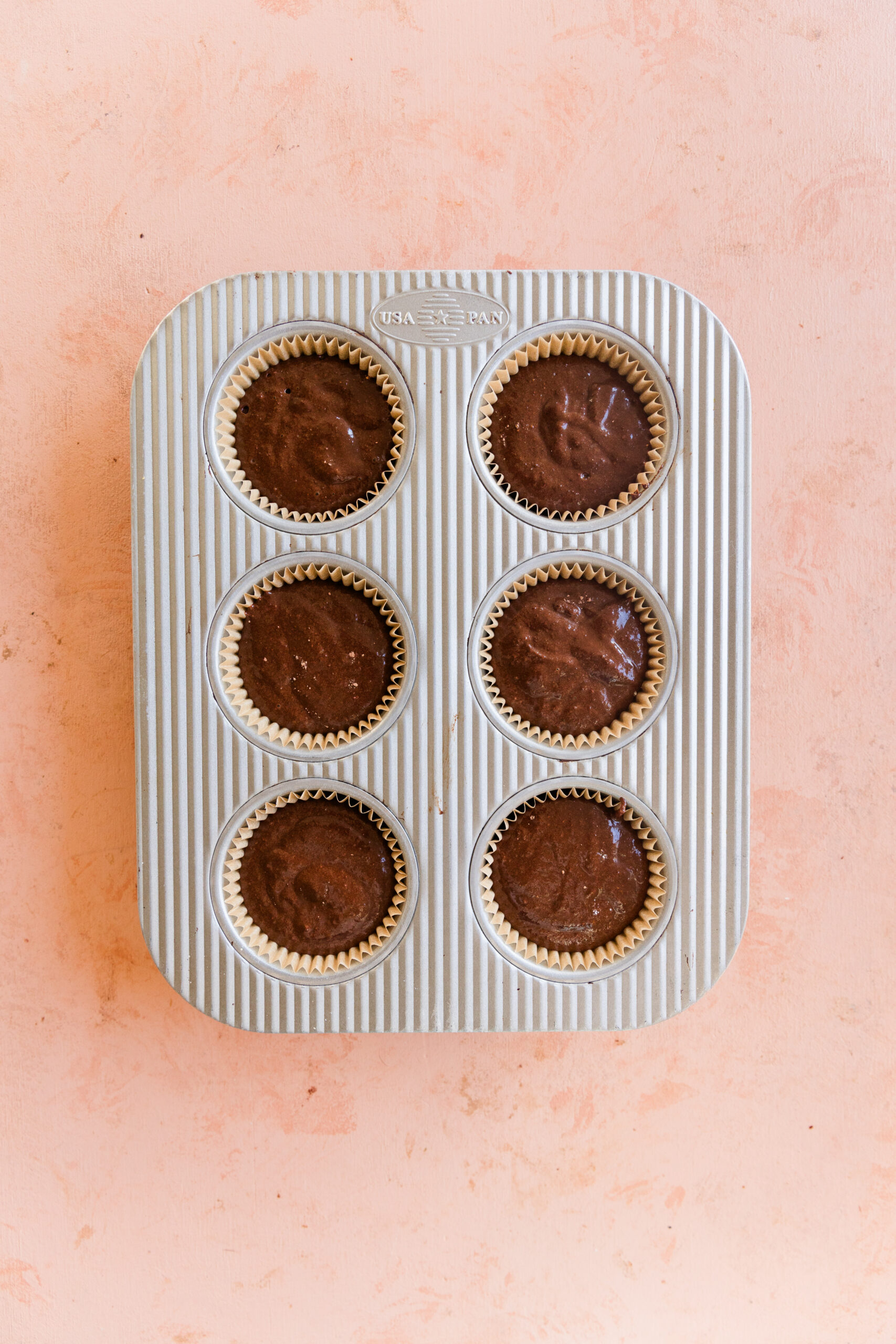 Chocolate cupcake batter in parchment paper lined cupcake tin.