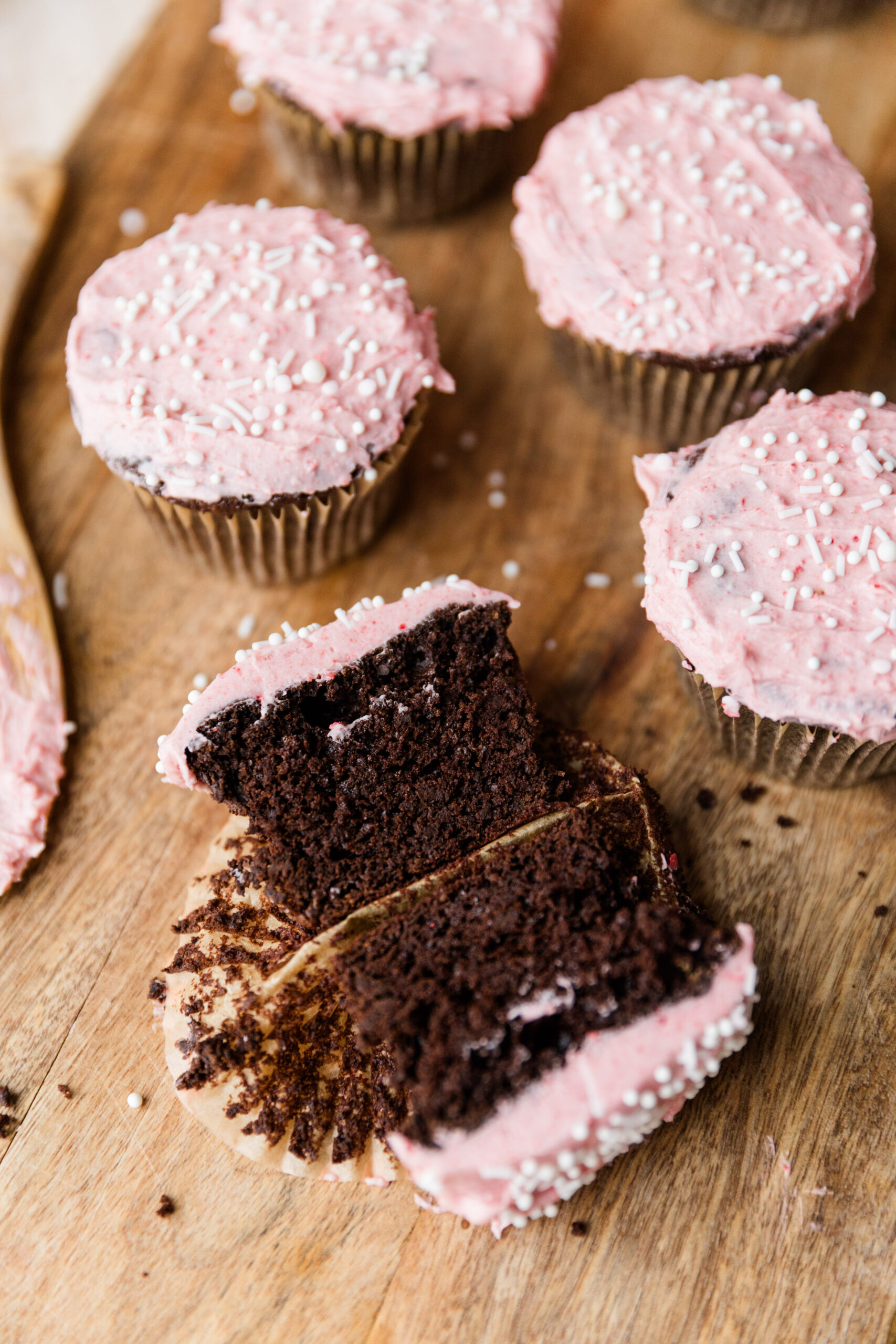 Chocolate cupcakes with pink frosting on a wooden board.